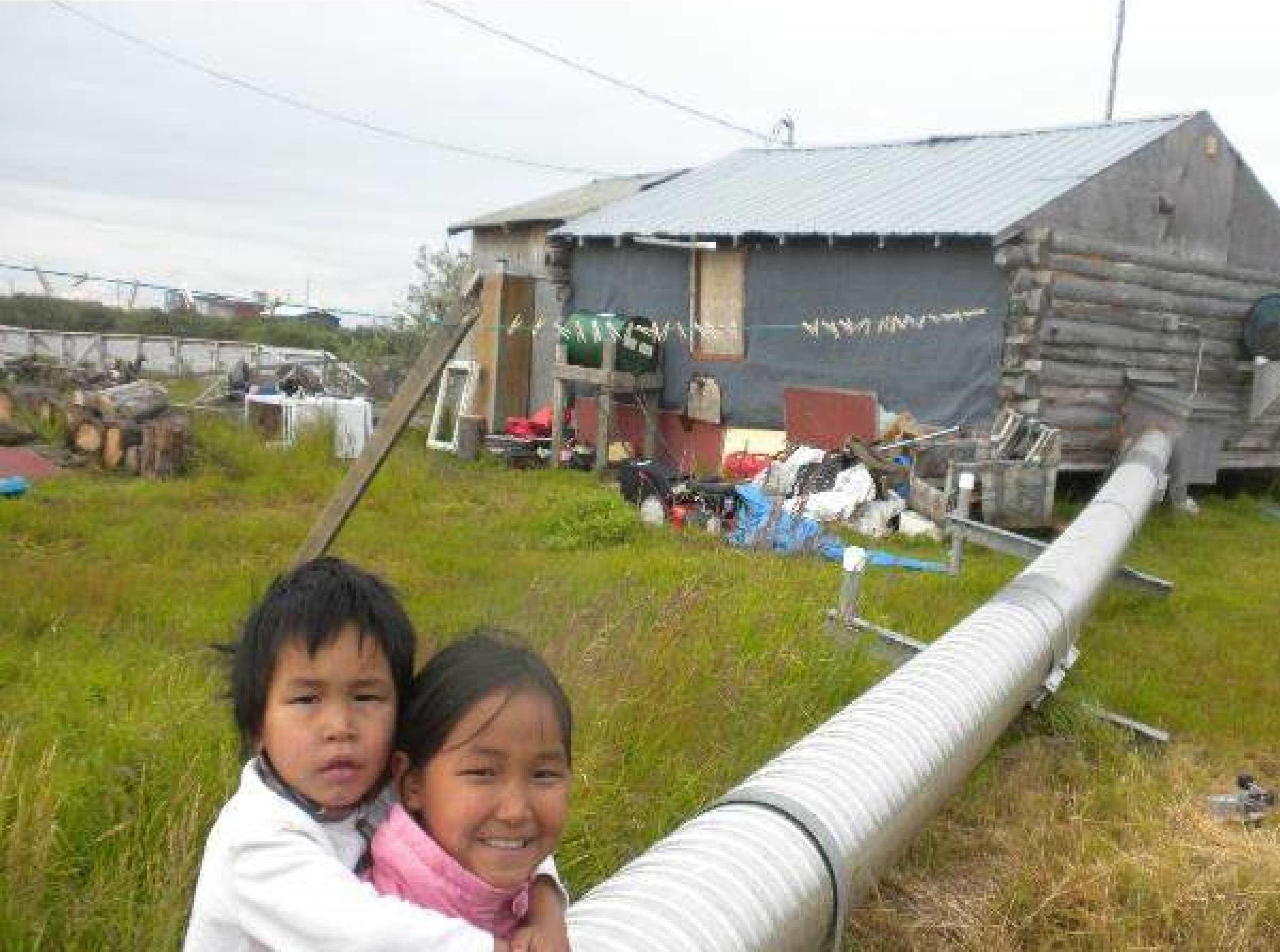 Figure 1 A woman and child smiling at the camera in a rural area, in background can be seen a pipeline connected to a residence